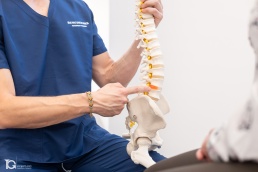 Iñaki Malo mostrando un modelo detallado de columna vertebral a una paciente en una sesión de fotografía corporativa en Pamplona