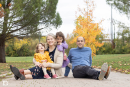 Fotografía familiar en Sarriguren con padres e hijas sentados en un camino del parque infantil.