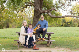 Fotografía familiar en Sarriguren con Liz y Jose junto a sus hijas sentados en una mesa del parque infantil.
