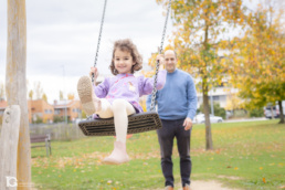 Fotografía familiar en Sarriguren de Ángela jugando en el columpio con su padre.