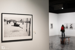 Fotograf&iacute;a Seminario de Ram&oacute;n Masats en primer plano, con personas observando la exposici&oacute;n al fondo